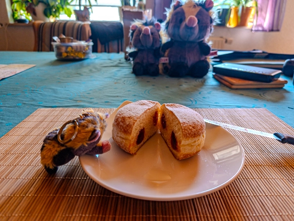 Ein halbierter Berliner Krapfen mit roter Marmeladenfüllung auf einem weißen Teller, daneben lehnt vergnügt Baby Viki.
